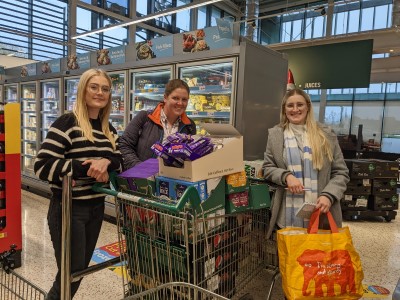 Abbey from the CFW team, Deborah from the Quality &amp; Impact team and Liss, Family Support Worker, standing in front of a trolley full of goodies in Morrisons Leamington Spa.