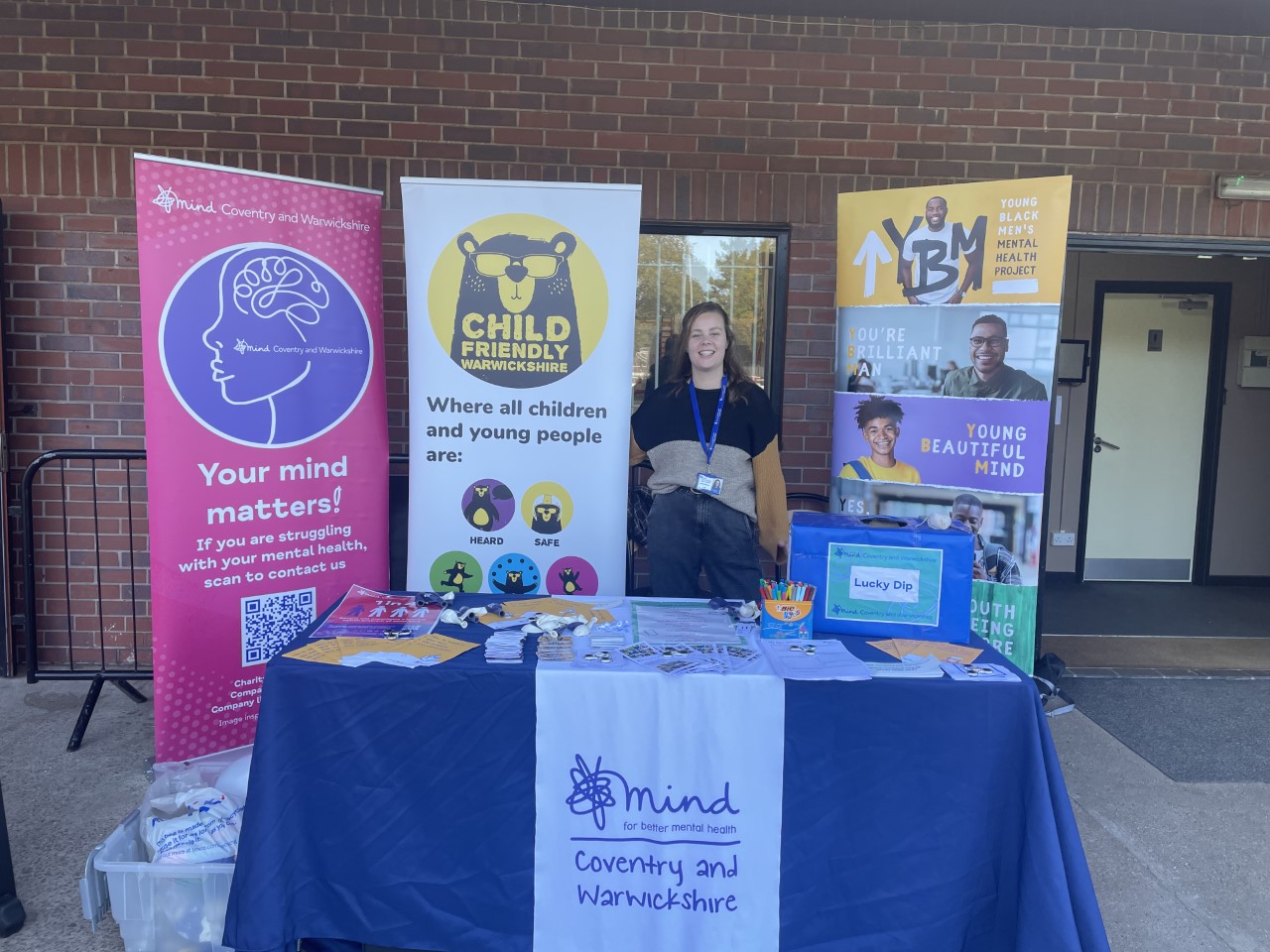 Photo of a CW Mind stall at the Wellbeing Festival, with a CFW banner and Young Black Men's MH banner in the background.